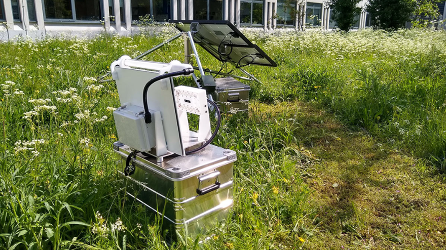 En ljusfälla står i en ängsmiljö utanför en kontorsbyggnad