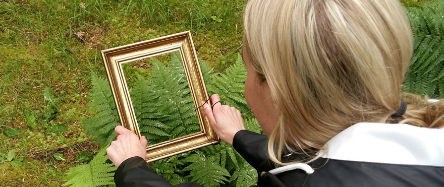 Kvinna som håller tavelram mot ormbunke